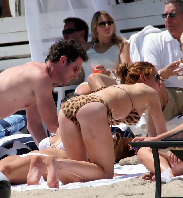 Lindsay Lohan resting barefoot on a beach in a leopard-print swimsuit.