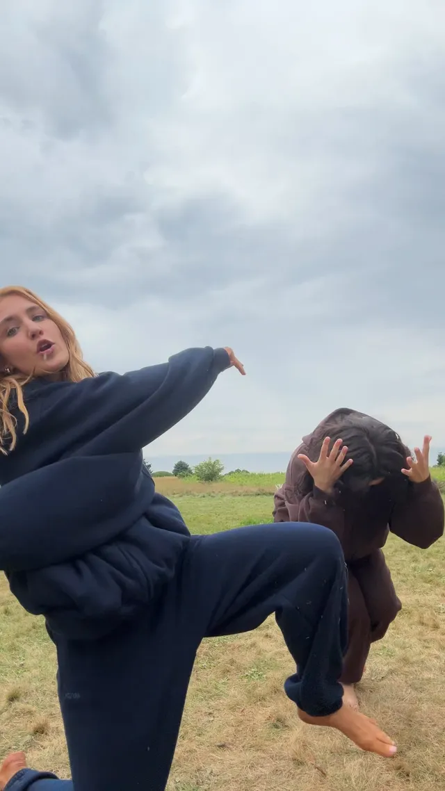 Sophie Nélisse jumping barefoot on grass beside another woman.