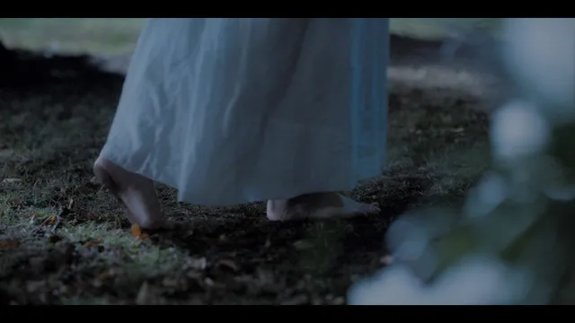 Phoebe Dynevor walking barefoot across a forest floor in a film scene.