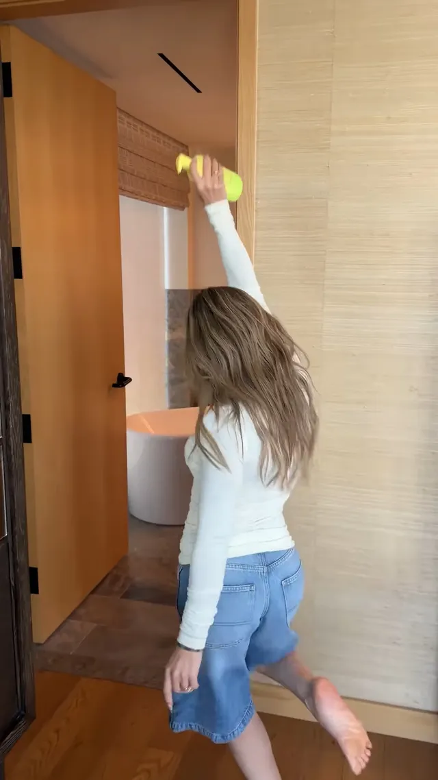 Hilary Duff standing barefoot beside a doorway in denim shorts.
