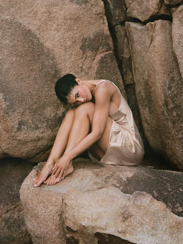Kylie Jenner sitting barefoot among large rocks.