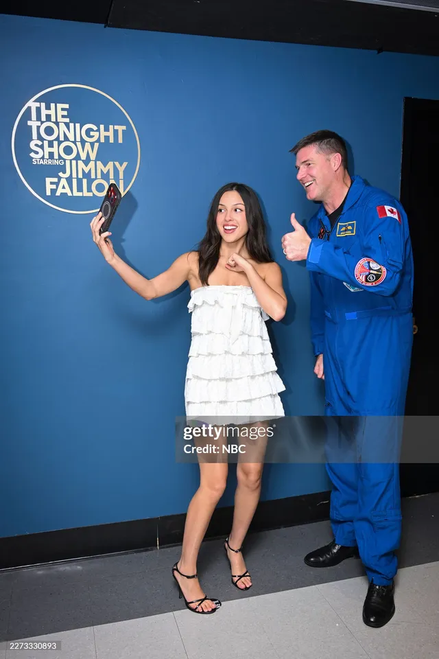 Olivia Rodrigo taking a selfie beside a man wearing a white dress and heels.