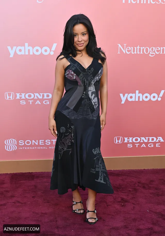 Cierra Ramirez in a black satin dress and heeled sandals on a pink event carpet.