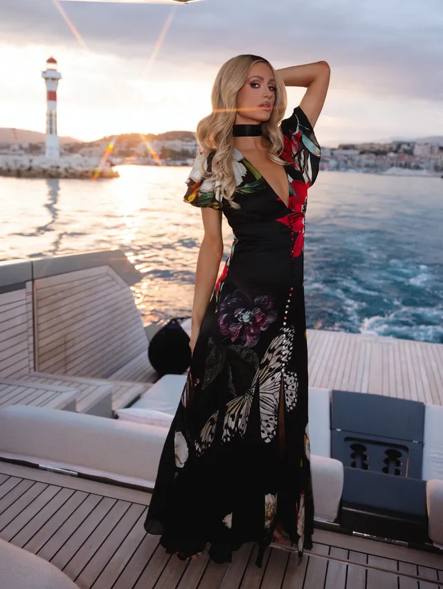 Paris Hilton standing on a boat in a black floral dress.