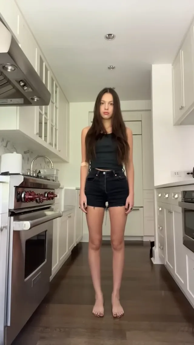 Olivia Rodrigo: standing barefoot in a kitchen in a black outfit.