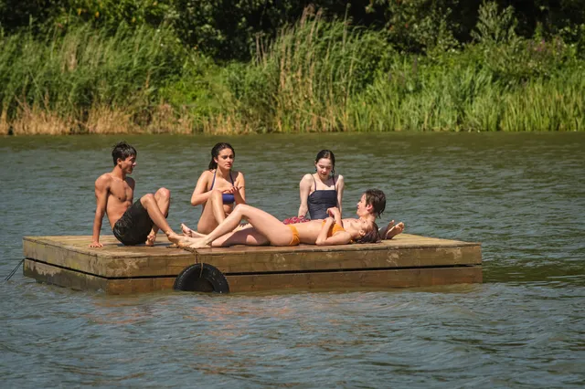 Emma Myers sitting barefoot with a group on a floating platform.