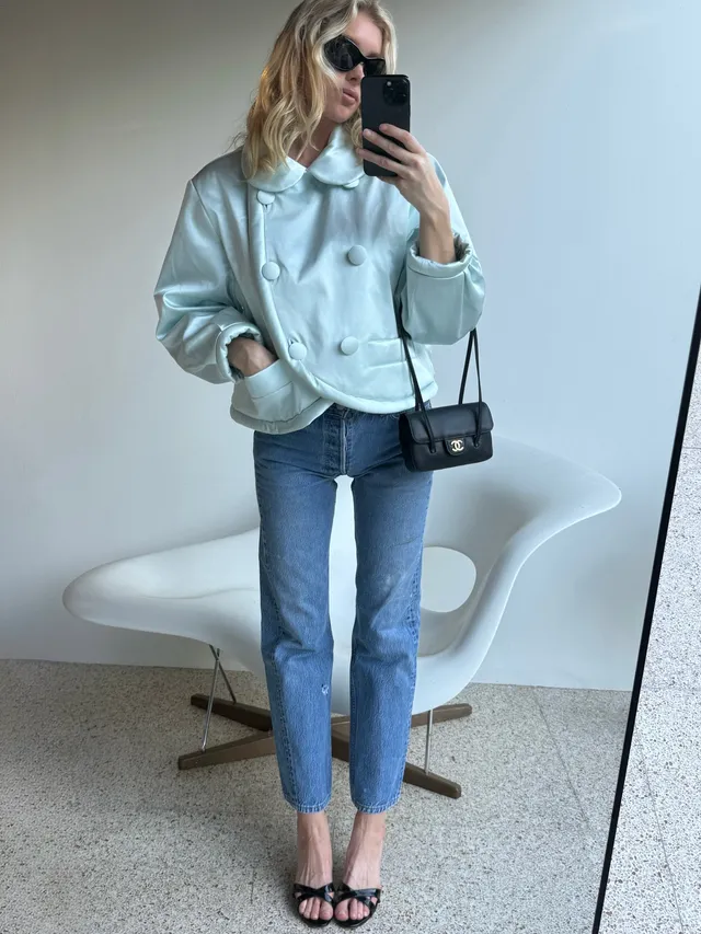 Elsa Hosk taking a mirror photograph in a pale jacket, jeans and black heeled sandals.