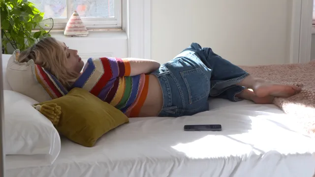 Peyton List lying barefoot on a bed in a striped top.