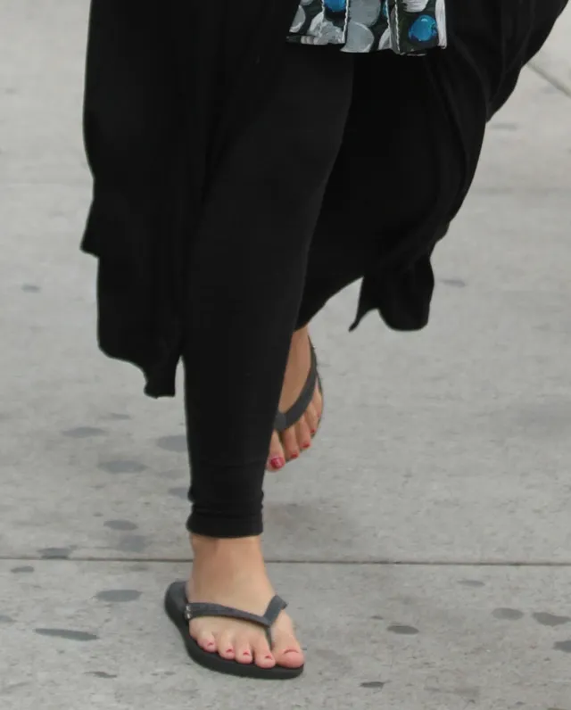 Leighton Meester walking on a pavement in dark trousers and flip-flops.