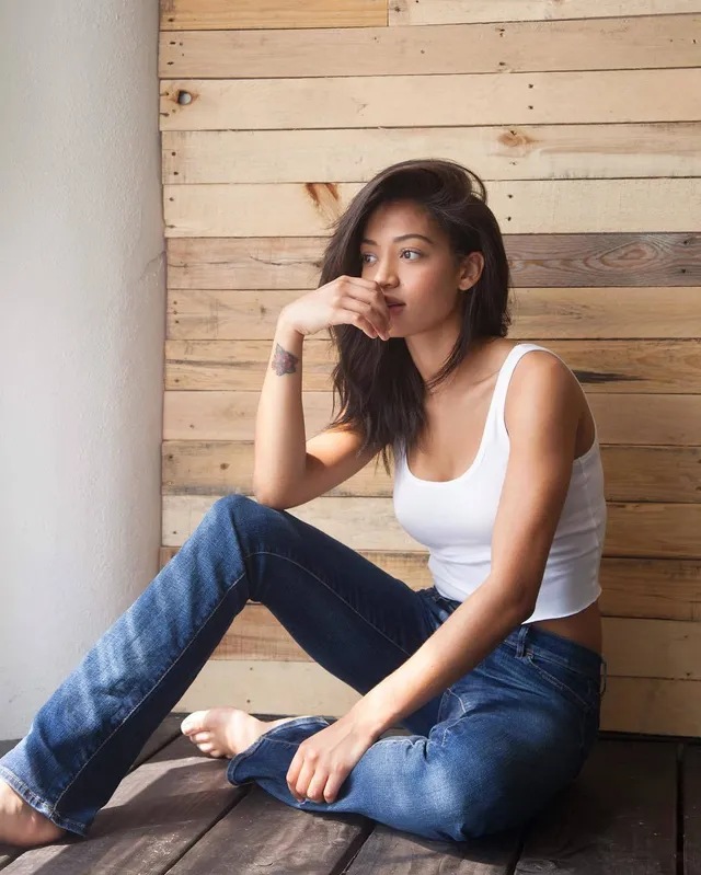 Samantha Logan sitting barefoot on a wooden bench in jeans and a white top.