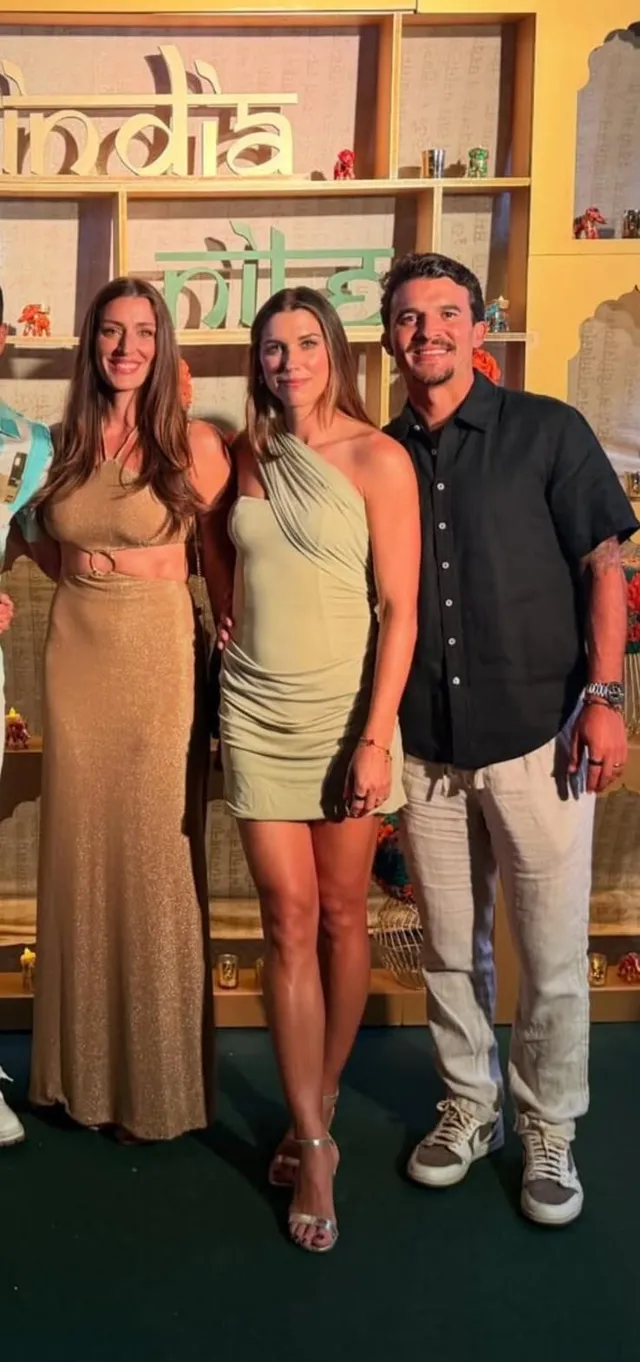 Alex Morgan wearing metallic heeled sandals and a pale dress with companions at an event.