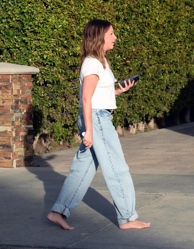 Ashley Tisdale walking barefoot in jeans and a white T-shirt.