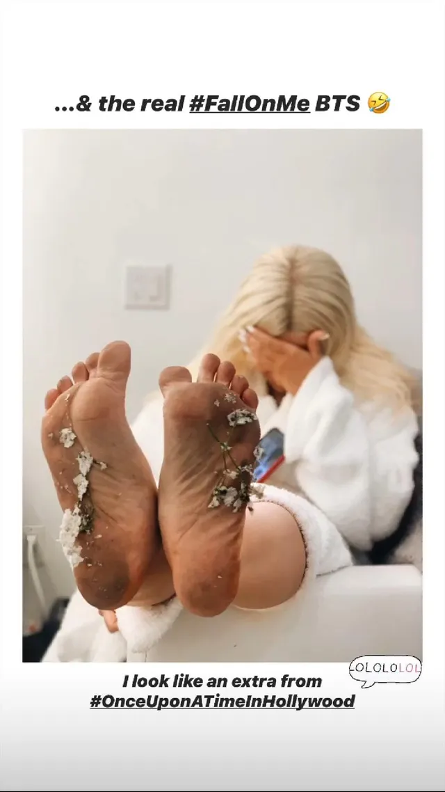 Christina Aguilera resting her bare soles toward the camera beneath a white outfit.