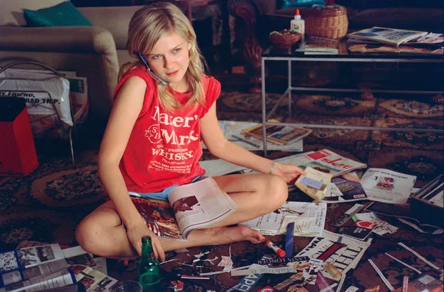 Kirsten Dunst sitting on the floor in a red top among magazines.