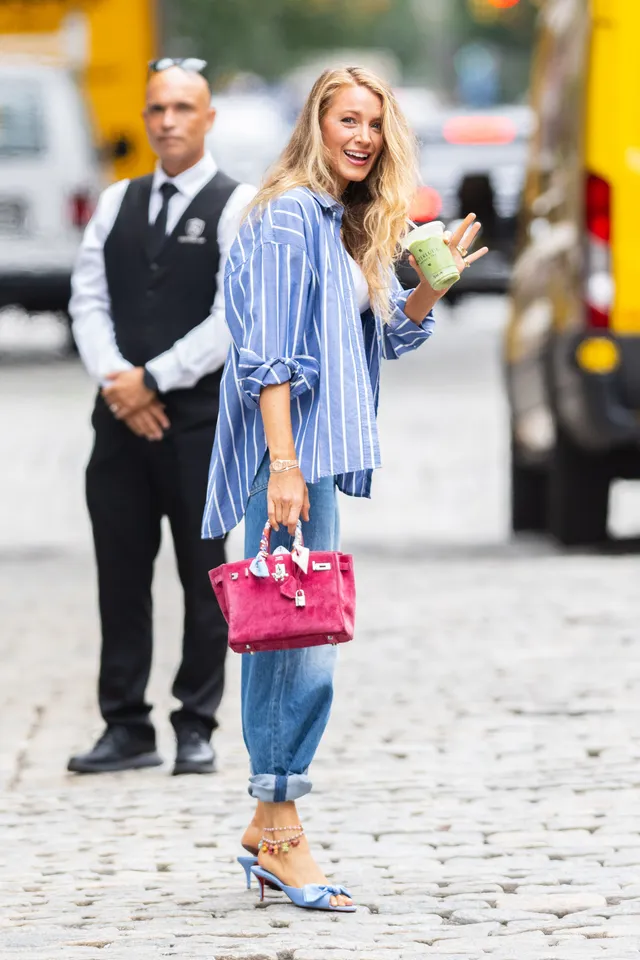 Blake Lively walking outdoors in a striped shirt and blue heels.