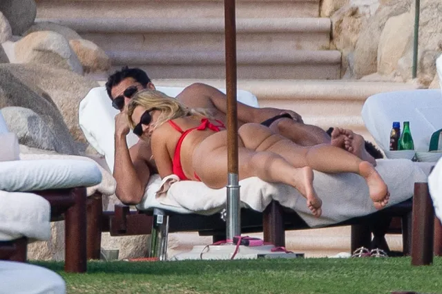 Bebe Rexha reclining barefoot on a sun lounger beside another adult.