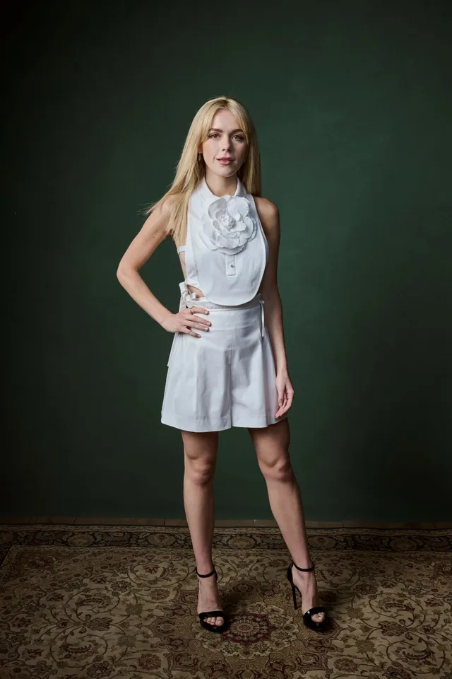 Kiernan Shipka standing in a pale outfit and black heels for a studio portrait.