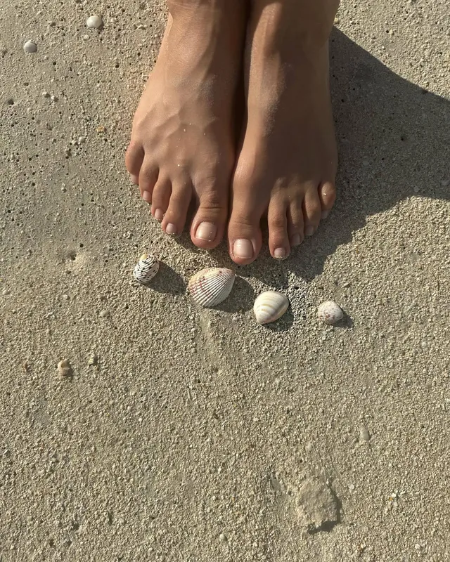 Irina Shayk bare feet beside shells on the sand.