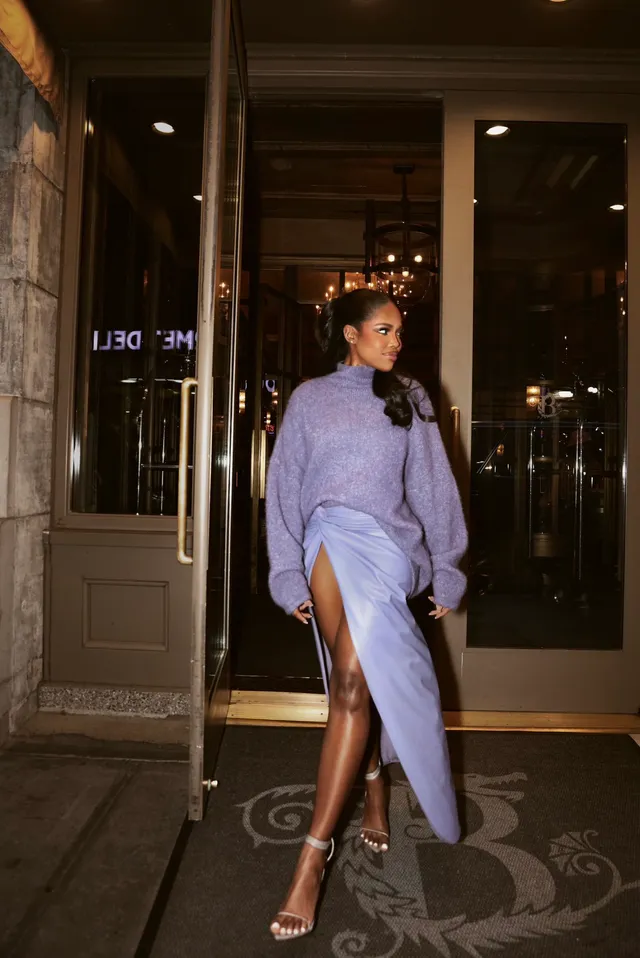 Ryan Destiny walking through a doorway in a lavender dress and clear heels.