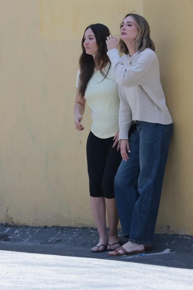 Kaley Cuoco standing beside another person while wearing flip-flops.