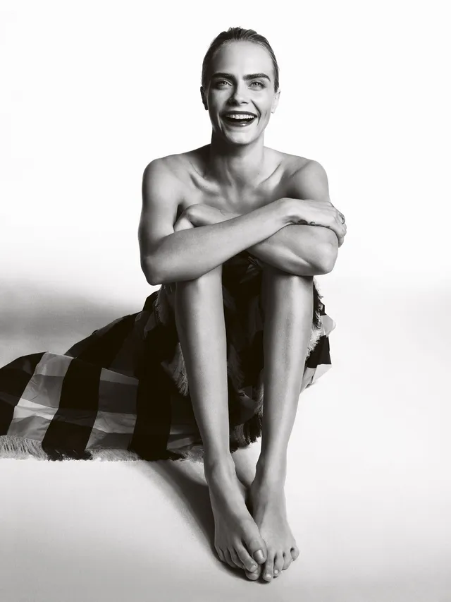 Cara Delevingne sitting with her knees raised in a monochrome portrait.
