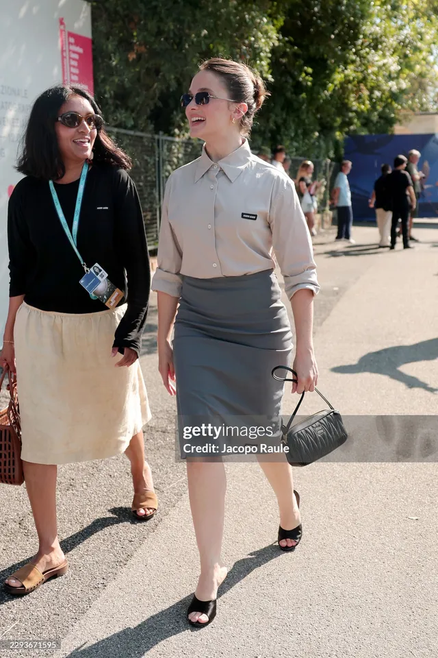 Cailee Spaeny walking beside another woman in a grey skirt and heels.