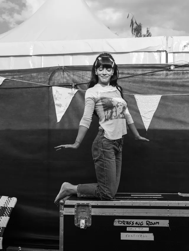 Lily Allen kneeling on a backstage equipment case.