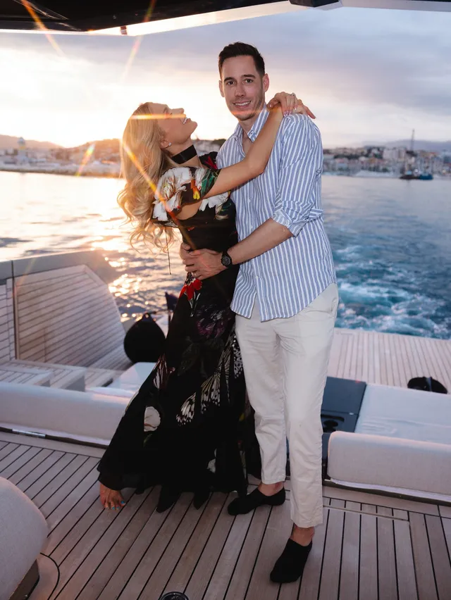 Paris Hilton standing beside a companion on a boat in a floral dress.