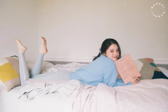 Han So-hee reading barefoot on a bed.