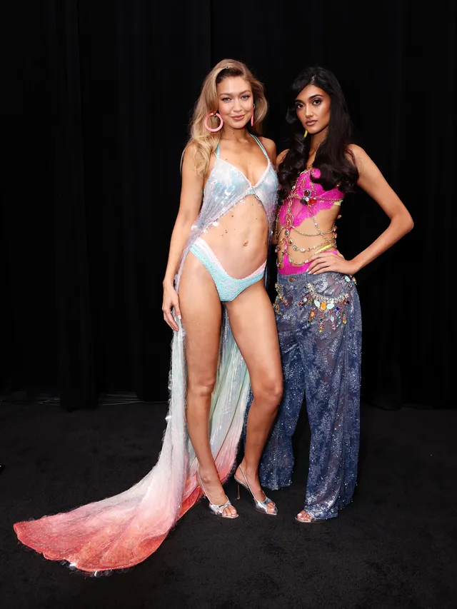 Gigi Hadid posing with another model in a winged outfit and heels.