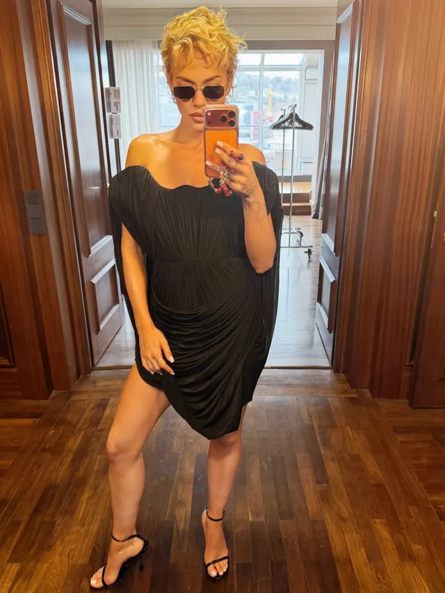Rita Ora taking a mirror photograph in a black dress and heels.