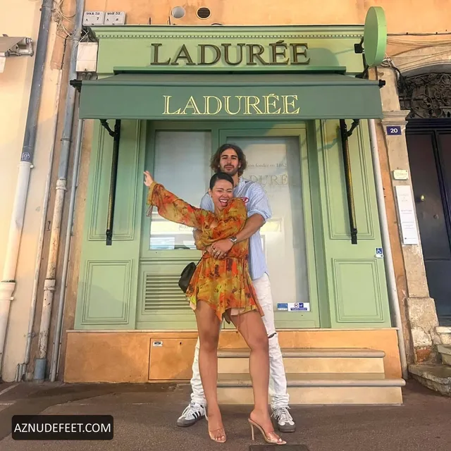 Cierra Ramirez in an orange patterned outfit and white feathered footwear outside a café.