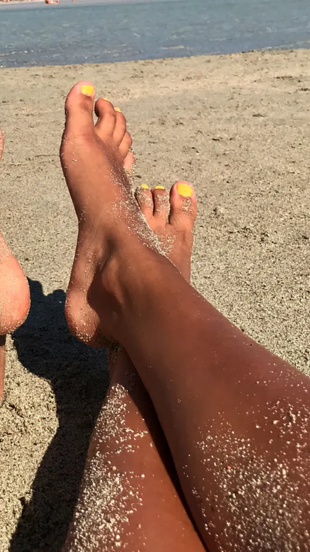 Ella Purnell relaxing on a sandy beach with bright nail polish.
