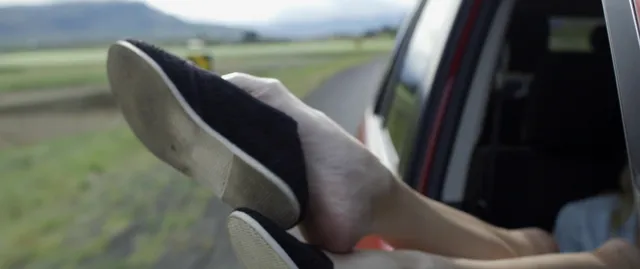 Maika Monroe resting a bare foot by a vehicle window in a scene.