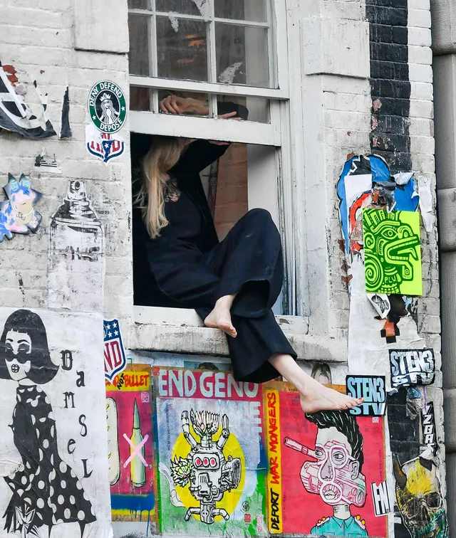Angelina Jolie seated in a window above a wall of posters.