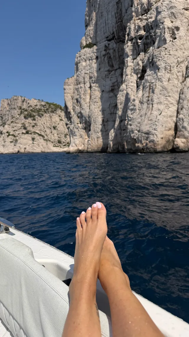 Sarah Michelle Gellar resting crossed bare feet on a boat beside rocky cliffs.