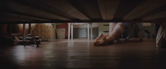 Chloë Grace Moretz with bare feet extended under a bed in a screen image.
