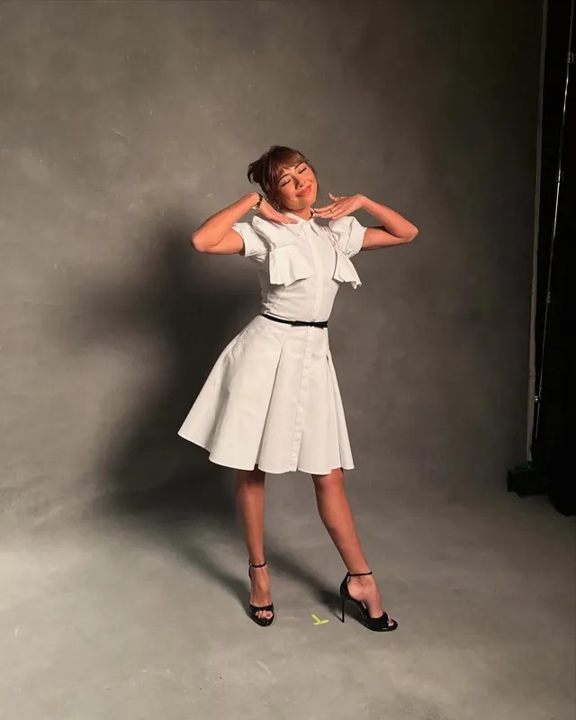 Xochitl Gomez posing in a pale outfit and black heels against a studio backdrop.