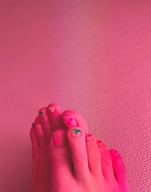 Jisoo showing pink-painted toenails against a pink background.