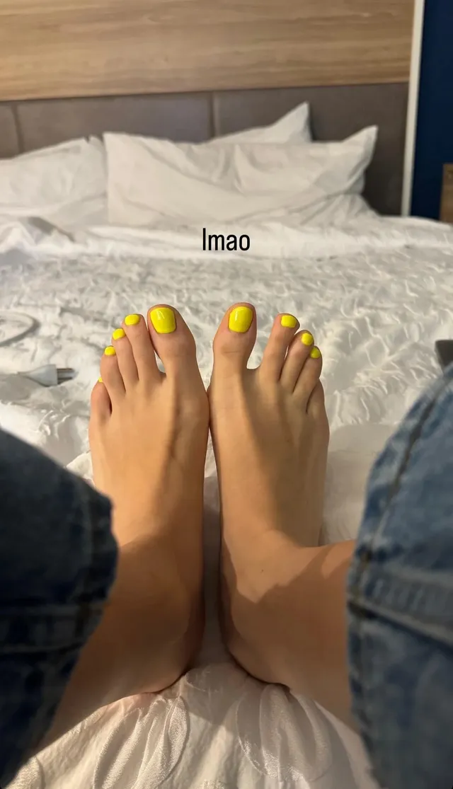 Eugenie Bouchard showing her bare feet with yellow-painted toenails on a bed.