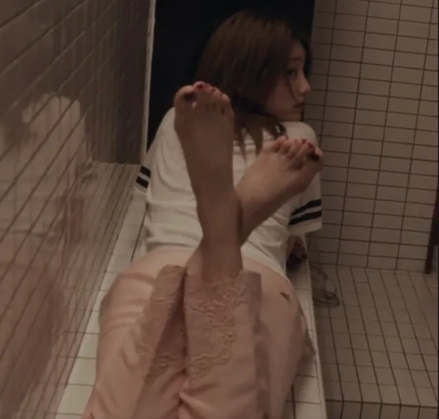 Bae Suzy raising bare feet beside a tiled wall in a scene.