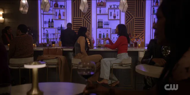 Greta Onieogou standing indoors in a red top, pale trousers and heels in a scene.
