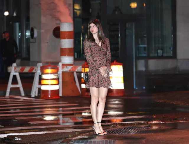 Alexandra Daddario walking outdoors in a patterned dress and black heels.