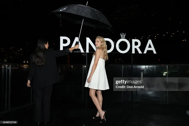 Teresa Palmer standing beside an event backdrop in a white dress.