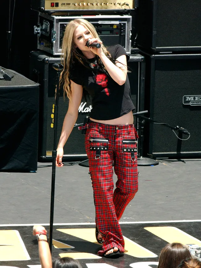 Avril Lavigne singing on stage in red trousers and flat sandals.