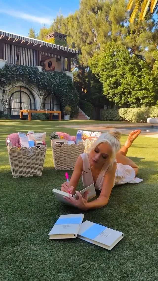 Christina Aguilera lying on grass beside open books with her bare soles raised.