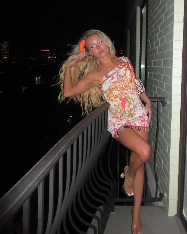 Zara Larsson posing on a balcony in a floral outfit and heels.