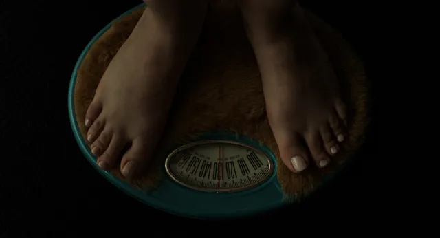 Cailee Spaeny standing barefoot on a bathroom scale in a film scene.