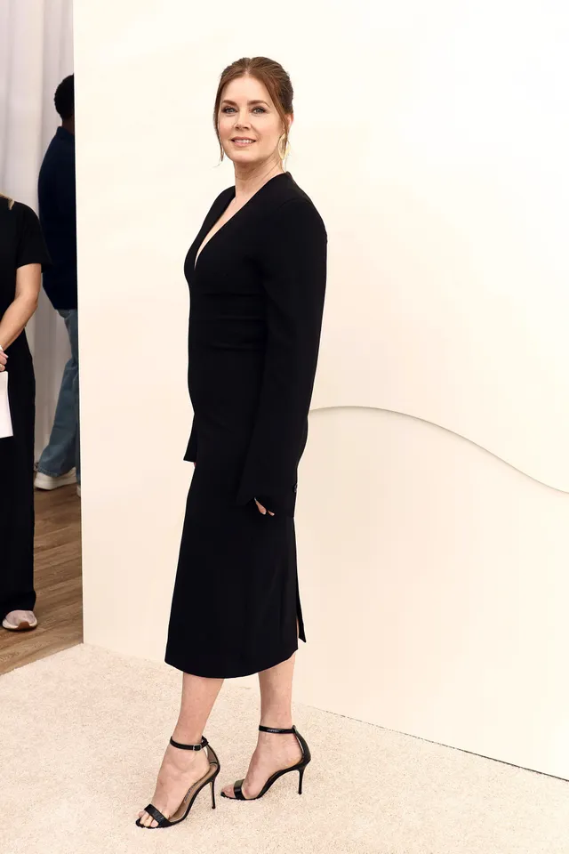 Amy Adams standing at an event in a fitted black dress.