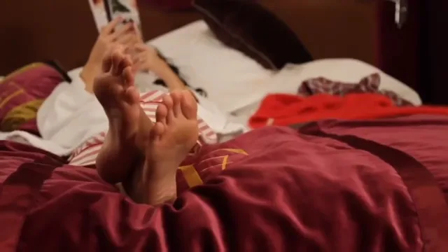 Katy Perry reclining on a bed with bare soles raised.